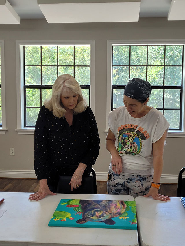 Photo of Virginia telling member Donna Barton about one of her paintings.