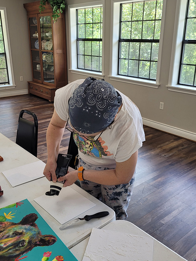 Photo of Virginia squeezing modeling paste from a tube onto her canvas panel.
